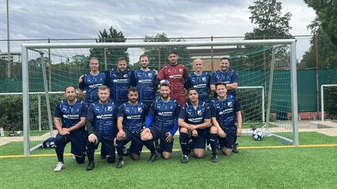 Gruppenfoto einer Fußballmannschaft in blauen Trikots vor einem Tor auf einem Kunstrasenplatz.