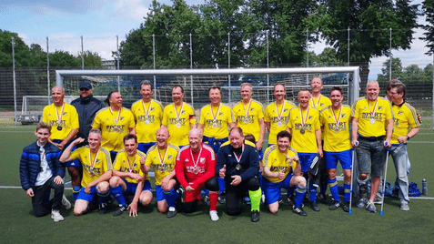 Mannschaftsfoto von Fußballspielern in gelben Trikots mit Medaillen auf einem Kunstrasenplatz.