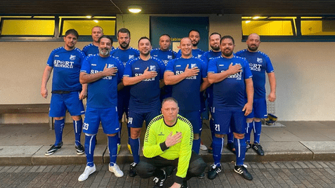 Gruppenfoto einer Fußballmannschaft in blauen Trikots, Männer stehen auf einer Treppe mit erhobenen Händen.