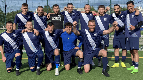 Mannschaftsaufstellung von 14 Fußballspielern auf einem Platz, alle in blauen Trikots mit weißen Streifen.