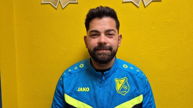 Porträt eines Mannes in blauer Sportjacke mit gelben Akzenten vor einer gelben Wand, mit Auszeichnung im Hintergrund.