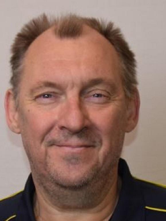 Porträt eines Mannes mit kurzem Haar, lächelnd, vor einem neutralen Hintergrund. Trägt ein dunkelblaues Poloshirt.