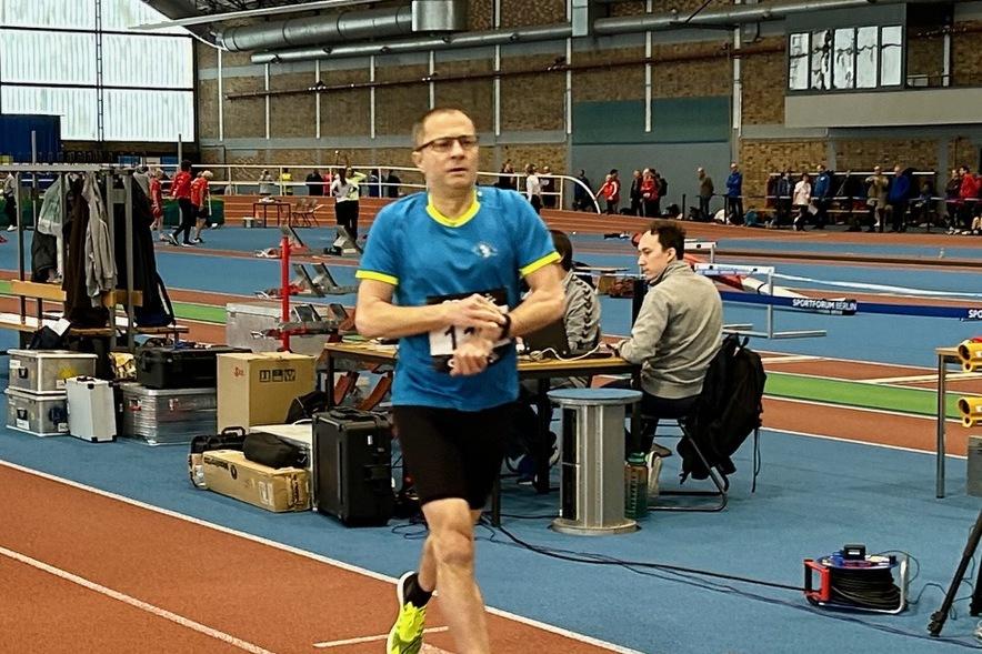 Ein Athlet in blauer Sportkleidung läuft auf einer Laufbahn in einer Sporthalle während eines Wettkampfs.