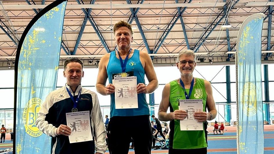 Drei Sportler stehen auf dem Siegertreppchen, halten Urkunden und tragen Medaillen bei einer Leichtathletik-Veranstaltung.