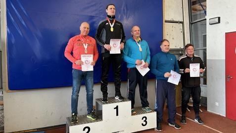 Fünf Sportler stehen auf dem Siegerpodest, halten Urkunden und Medaillen in der Hand. Blaues Paspellierungs-Hintergrund.