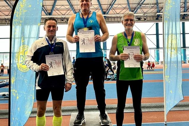 Drei Sportler stehen auf dem Siegertreppchen, halten Urkunden und tragen Medaillen bei einer Leichtathletik-Veranstaltung.