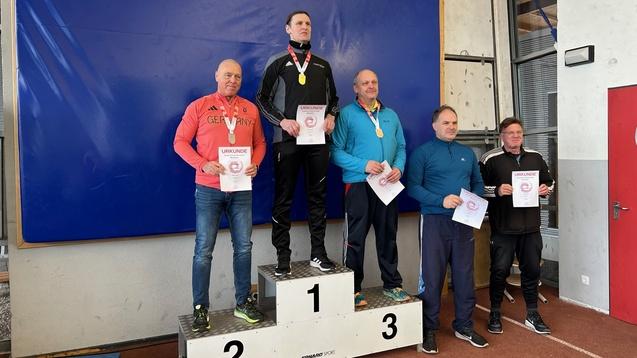 Fünf Sportler stehen auf dem Siegerpodest, halten Urkunden und Medaillen in der Hand. Blaues Paspellierungs-Hintergrund.