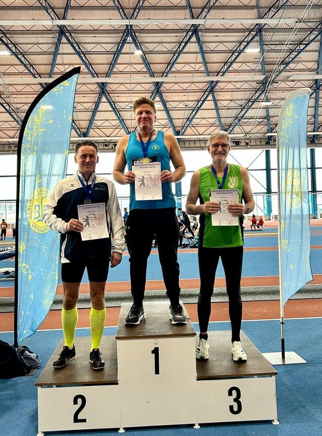 Drei Medaillenträger stehen auf dem Siegerpodest mit Urkunden in der Hand in einer Sporthalle.