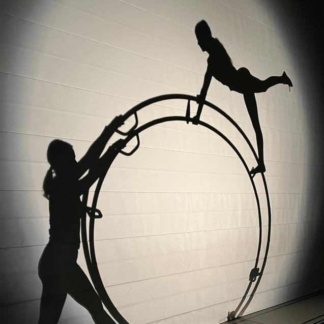 Schatten von zwei Personen, eine balanciert auf einem großen Ring, die andere hält ihn an der Seite.