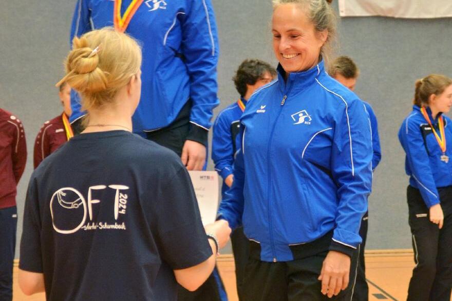 Zwei Sportlerinnen in blauen Trainingsjacken auf dem Siegertreppchen, eine erh&auml;lt eine Urkunde von einer anderen.