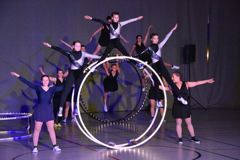 Akrobatische Darbietung mit Tänzern auf Reifen und in Schwarz-Weiß-Kleidung auf einer Bühne mit Beleuchtung.