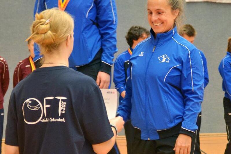 Zwei Sportlerinnen in blauen Trainingsjacken auf dem Siegertreppchen, eine erh&auml;lt eine Urkunde von einer anderen.