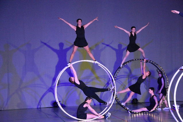 Vier Artistinnen in Schwarz balancieren in verschiedenen Positionen auf drei gro&szlig;en Reifen auf einer B&uuml;hnenfl&auml;che.