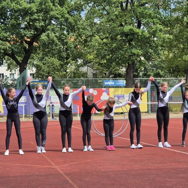 Gruppe von Turnerinnen in einheitlichen Outfits, die sich auf einem Sportplatz dem Publikum präsentieren.