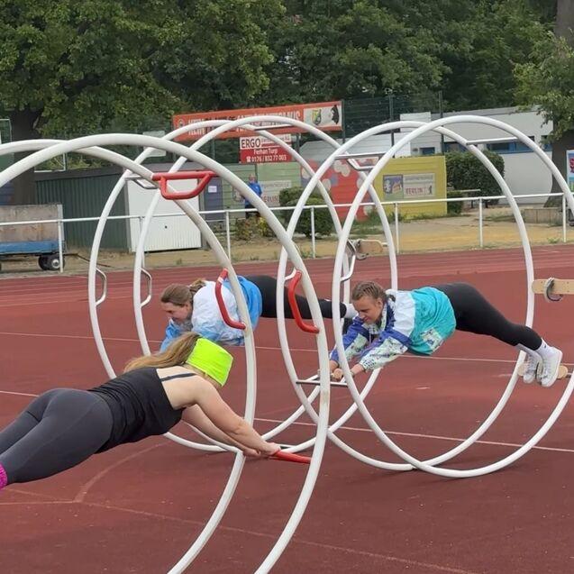Drei Frauen trainieren in einem Sportpark in großen Reifen auf einer Laufbahn.