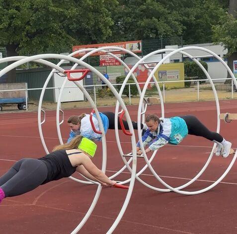 Drei Frauen trainieren in einem Sportpark in großen Reifen auf einer Laufbahn.