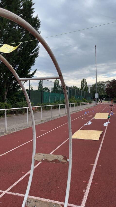 Blick auf eine Sportarena mit einer Laufbahn, Hindernissen und Bäumen im Hintergrund unter bewölktem Himmel.