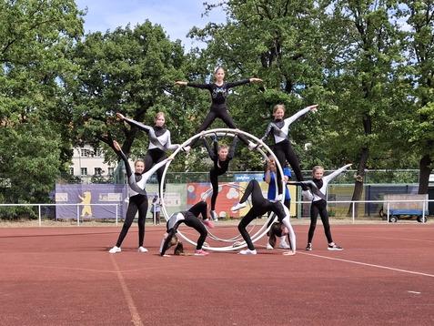 Gruppierung von Kindern in schwarzen Outfits, die auf Ringen stehen, auf einem roten Sportplatz vor Bäumen.