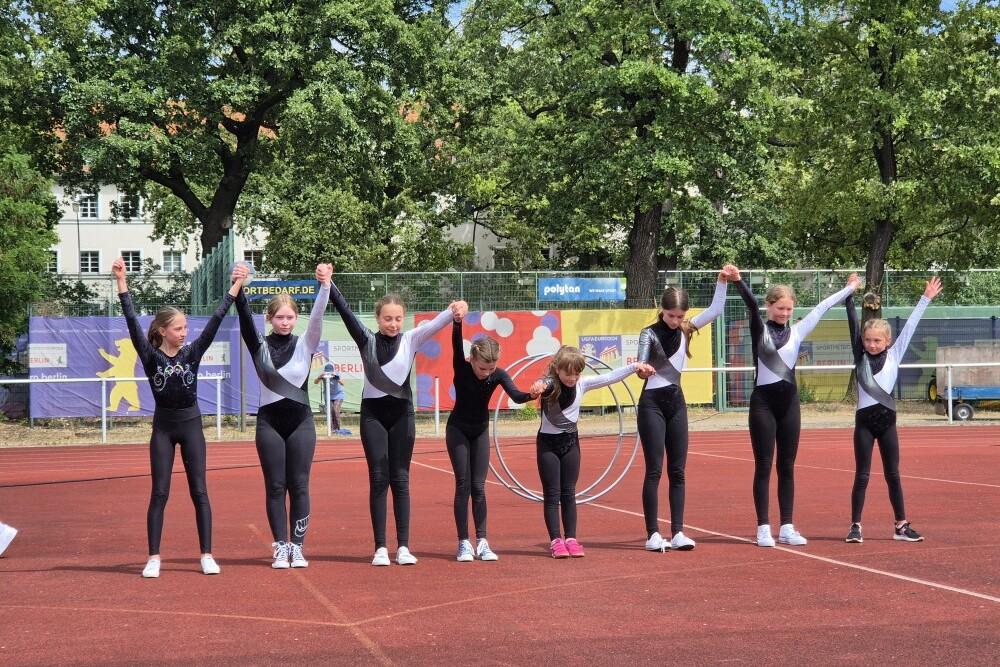 Gruppe von Turnerinnen in einheitlichen Outfits, die sich auf einem Sportplatz dem Publikum präsentieren.