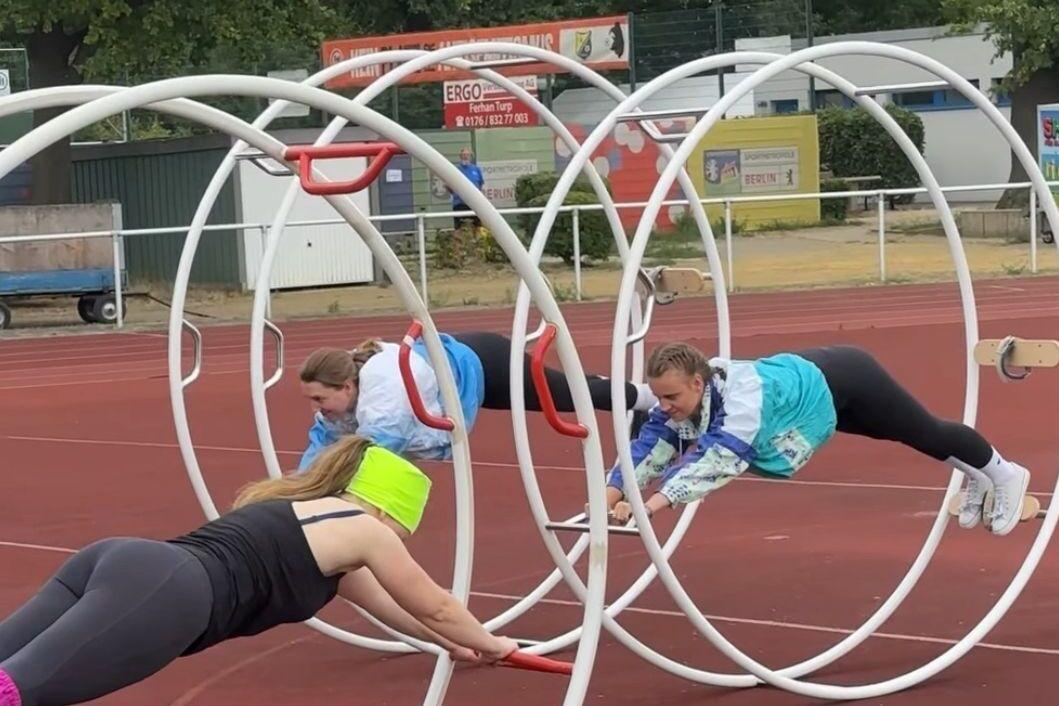 Drei Frauen trainieren in einem Sportpark in großen Reifen auf einer Laufbahn.