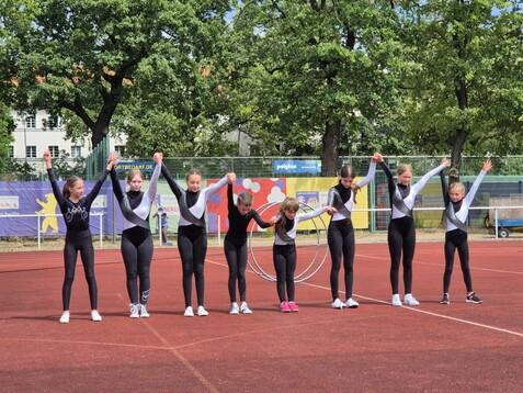 Gruppe von Turnerinnen in einheitlichen Outfits, die sich auf einem Sportplatz dem Publikum präsentieren.