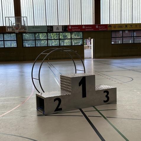 Podest mit den Zahlen 1, 2 und 3 sowie einem großen Reifen in einer sportlichen Halle.