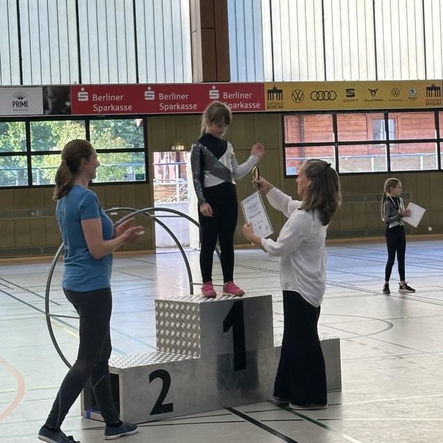 M&auml;dchen auf dem Siegertreppchen erh&auml;lt eine Urkunde w&auml;hrend einer Sportveranstaltung in einer Halle.