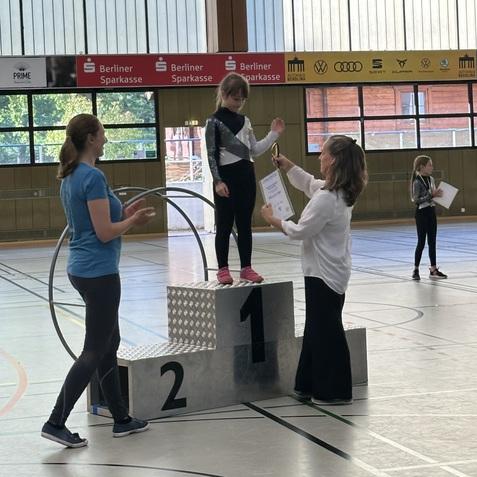 M&auml;dchen auf dem Siegertreppchen erh&auml;lt eine Urkunde w&auml;hrend einer Sportveranstaltung in einer Halle.