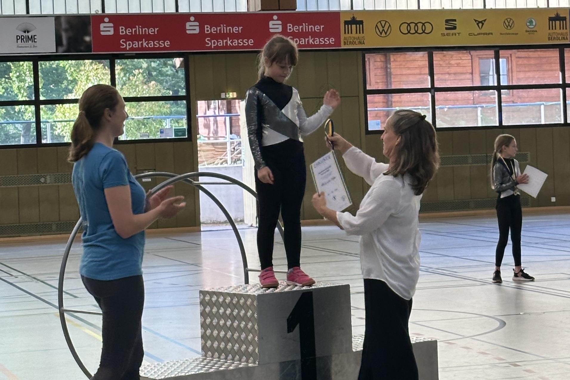 M&auml;dchen auf dem Siegertreppchen erh&auml;lt eine Urkunde w&auml;hrend einer Sportveranstaltung in einer Halle.