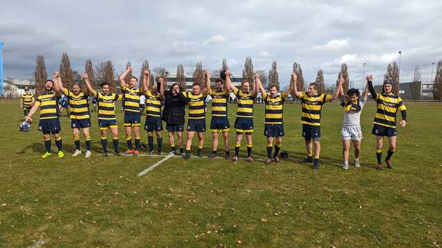 Eine Rugby-Mannschaft hält nach dem Spiel die Hände hoch, um den Sieg auf einem Grünfeld zu feiern.