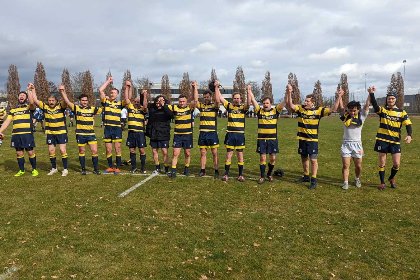 Eine Rugby-Mannschaft hält nach dem Spiel die Hände hoch, um den Sieg auf einem Grünfeld zu feiern.