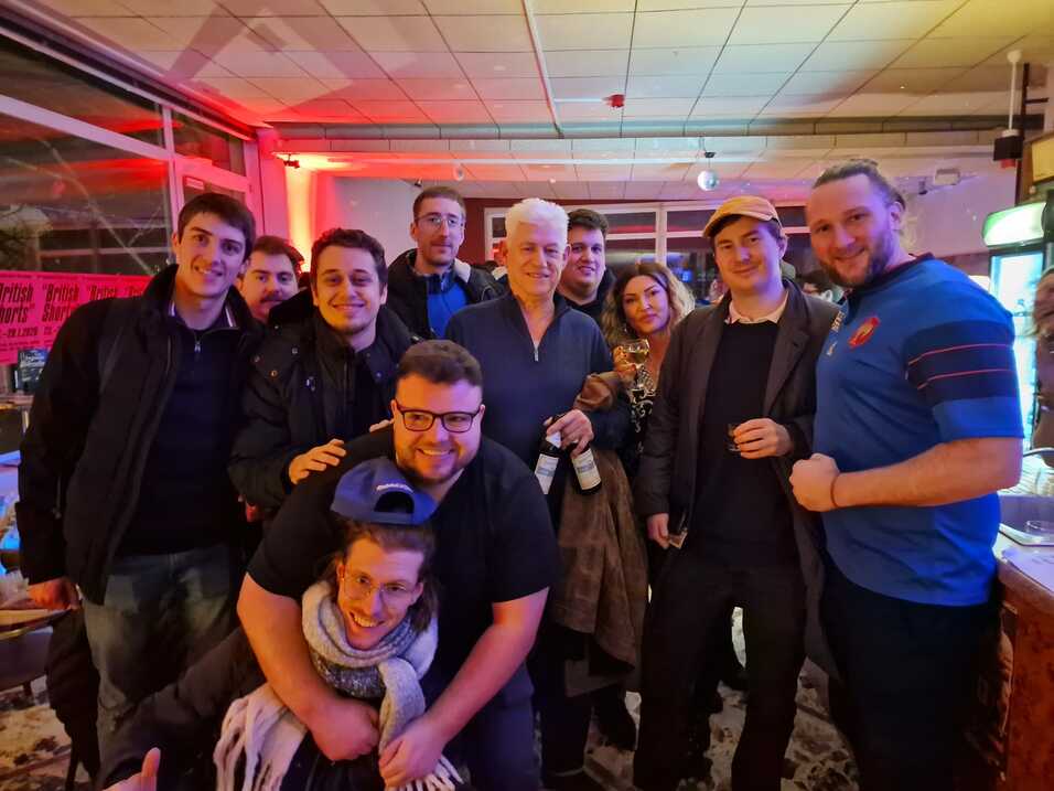 Gruppe von zehn Personen in einem Innenraum, teilweise lachend und mit Getränken, vor einer bunten Hintergrundbeleuchtung.