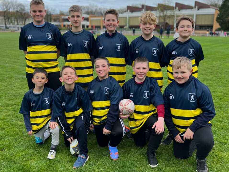 Gruppe von zehn Kindern in Rugby-Trikots mit gelben und blauen Streifen, lächeln auf einem Spielfeld.