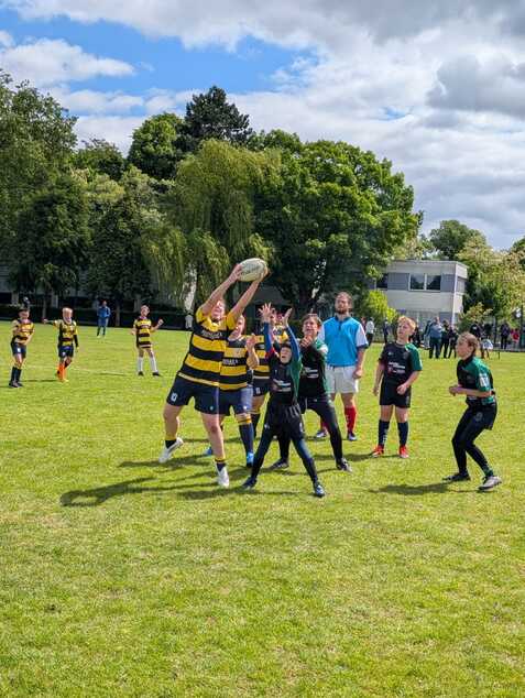 Kind in gelb-schwarz hebt den Rugby-Ball hoch, um einen Wurf während eines Spiels auf dem grünen Feld auszuführen.