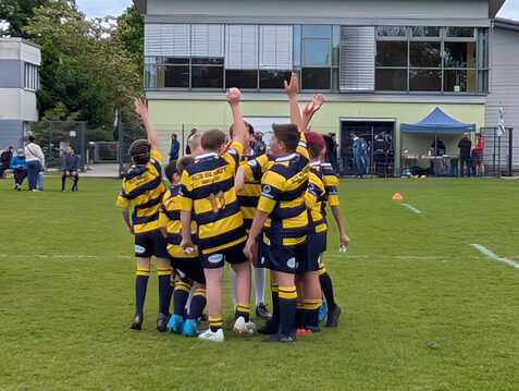 Kinder in gestreiften Rugbytrikots heben die Hände in die Luft, um ihren Teamgeist auf einem grünen Platz zu zeigen.