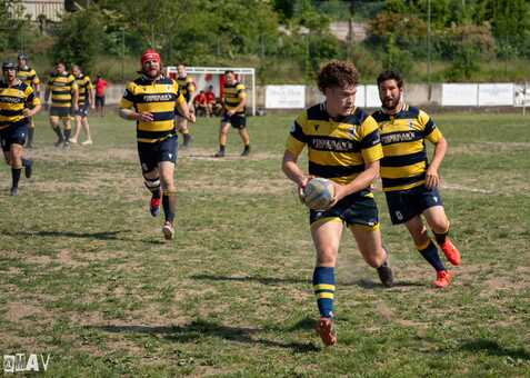 Rugbyspieler sprinten über das Feld, während einer den Ball in der Hand trägt. Alle tragen gestreifte Trikots.