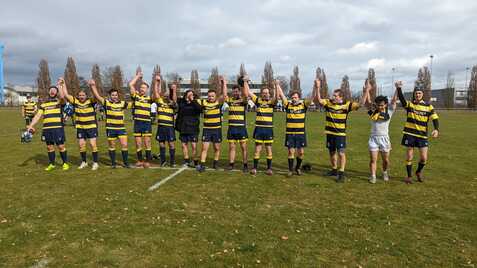 Eine Rugby-Mannschaft hält nach dem Spiel die Hände hoch, um den Sieg auf einem Grünfeld zu feiern.