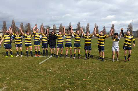 Eine Rugby-Mannschaft hält nach dem Spiel die Hände hoch, um den Sieg auf einem Grünfeld zu feiern.