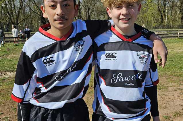 Zwei junge Fußballspieler stehen nebeneinander, tragen schwarze und weiße Trikots und lächeln in die Kamera.