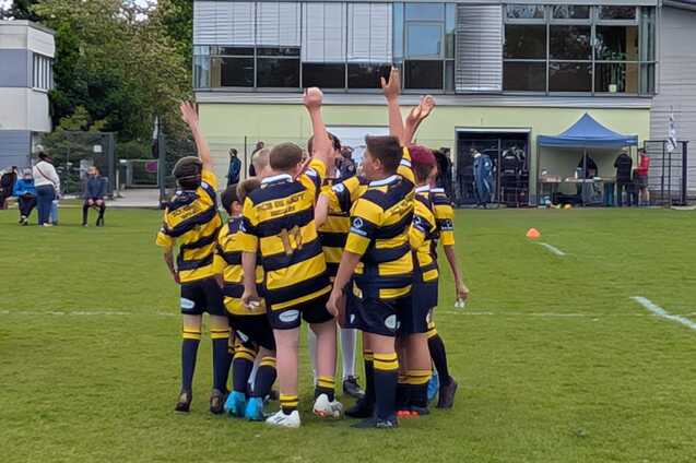 Kinder in gestreiften Rugbytrikots heben die H&auml;nde in die Luft, um ihren Teamgeist auf einem gr&uuml;nen Platz zu zeigen.
