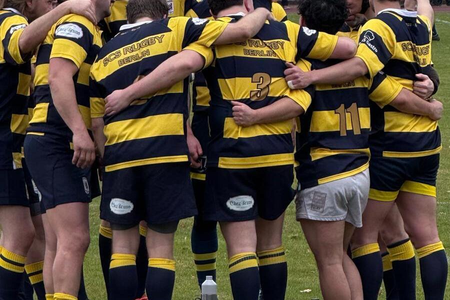 Rugbyteam in gelb-blauen Trikots umarmt sich, bereit f&uuml;r eine Besprechung auf dem Spielfeld.