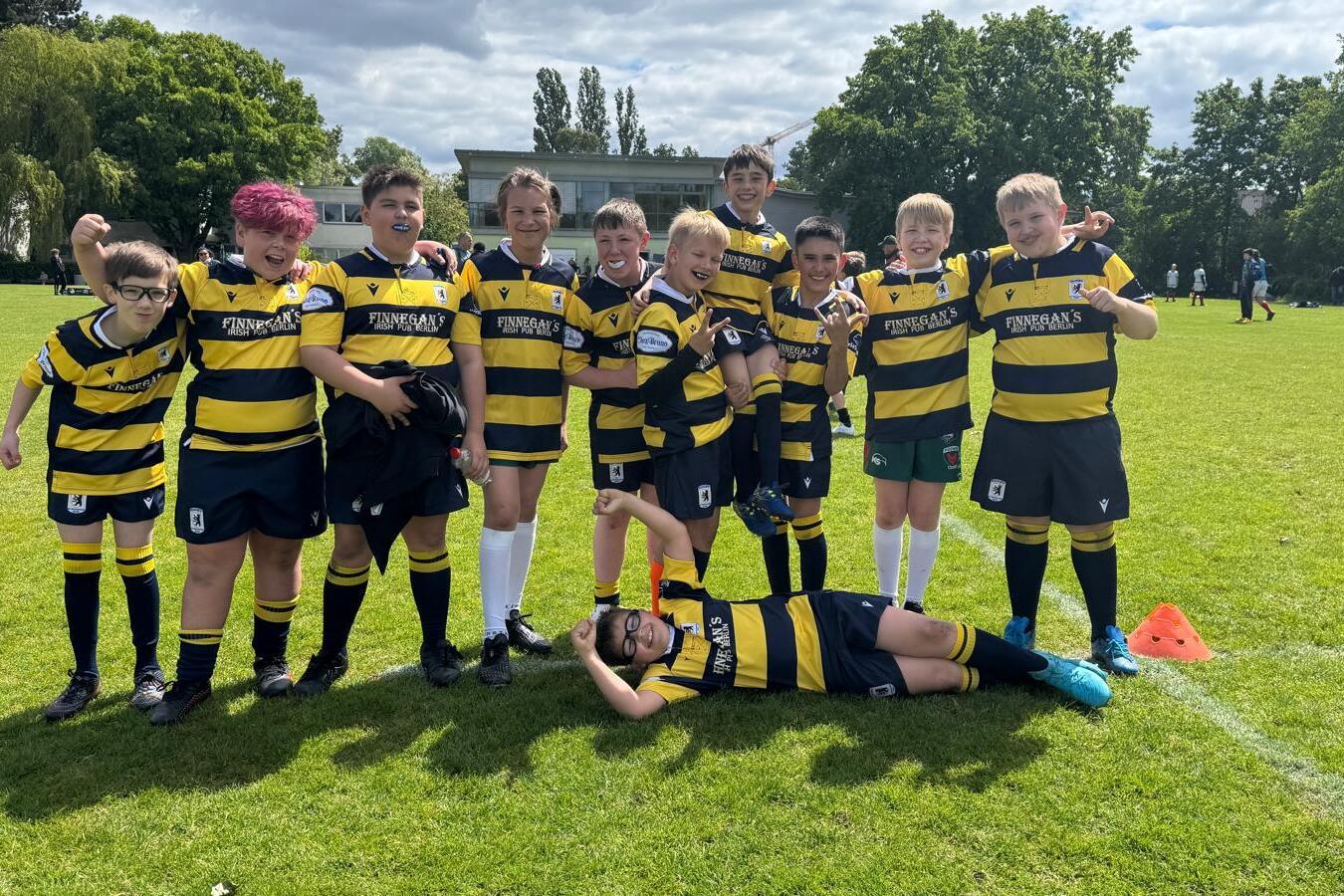 Gruppe von Kindern in gestreiften Rugby-Trikots posiert fr&ouml;hlich auf einem gr&uuml;nen Rasenfeld.