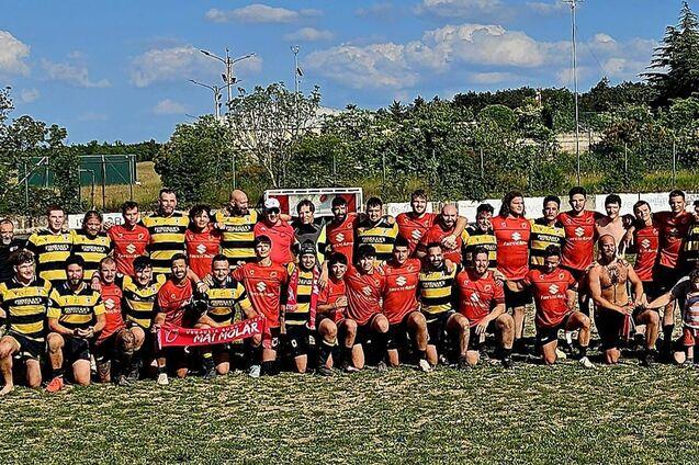 Gruppenfoto von Rugby-Spielern in roten und schwarzen Trikots sowie gelben und schwarzen Streifen, auf einem grünen Spielfeld.
