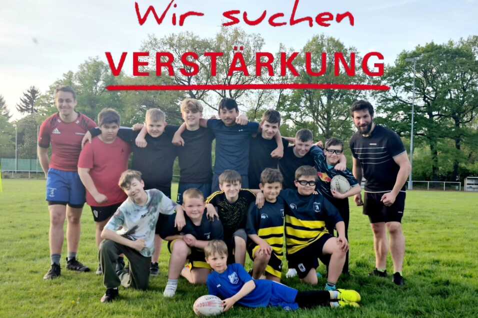 Gruppe von Kindern und Jugendlichen in Sportkleidung steht auf einem Rasen, ein Junge h&auml;lt einen Rugbyball.