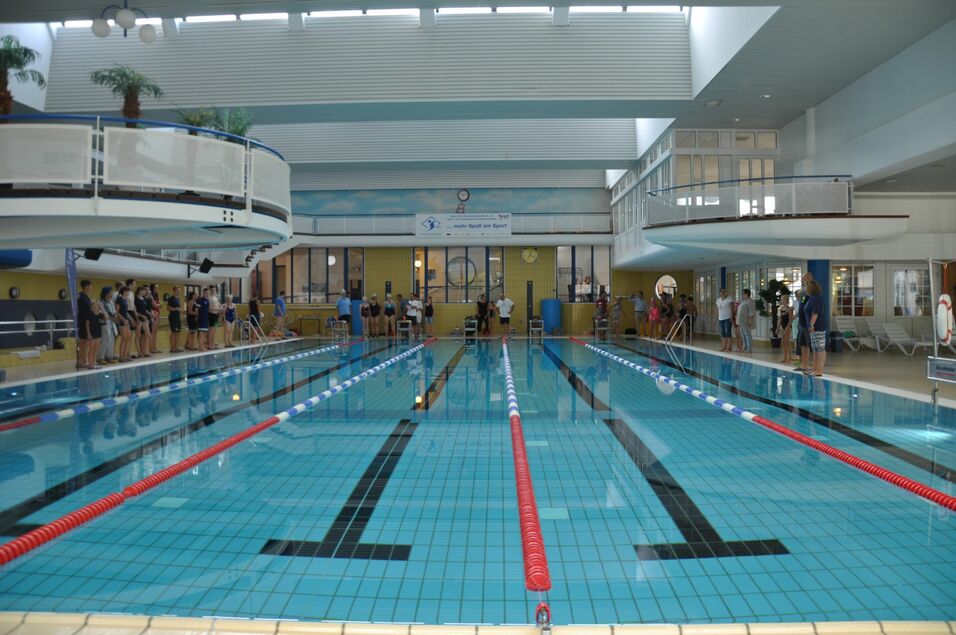 Innansicht eines Schwimmbads mit mehreren Sportlern, die sich am Beckenrand aufstellen.