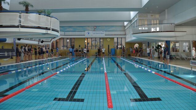 Innansicht eines Schwimmbads mit mehreren Sportlern, die sich am Beckenrand aufstellen.