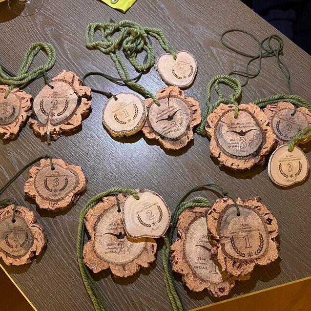 Mehrere Medaillen aus Holz liegen auf einem Tisch, beschriftet mit Zahlen und Wettbewerbsinformationen.