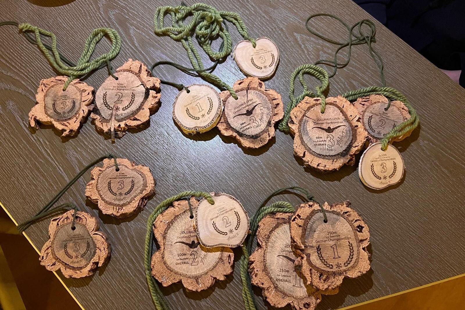 Mehrere Medaillen aus Holz liegen auf einem Tisch, beschriftet mit Zahlen und Wettbewerbsinformationen.