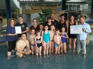 Gruppe von Kindern und Lehrern im Schwimmbad, posierend mit Urkunden und Auszeichnungen.