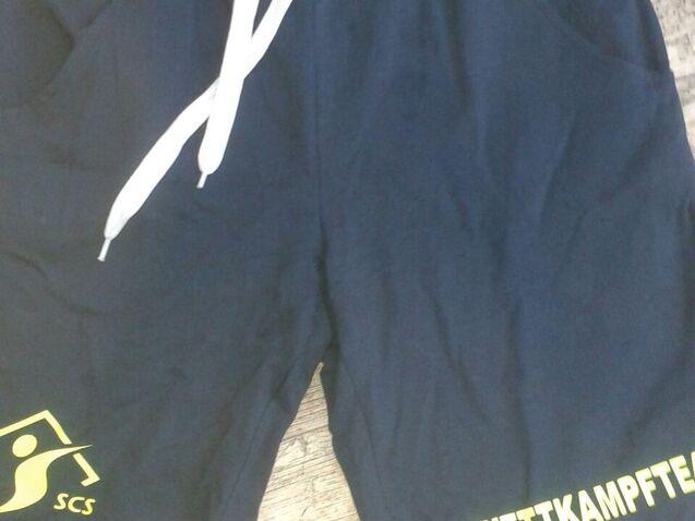 Navyfarbene Sportshorts mit wei&szlig;en Kordeln und gelbem Aufdruck &bdquo;WETTKAMPFTEAM&ldquo; am rechten Bein.